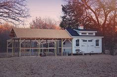 a white barn with a wooden roof in the middle of a field next to trees