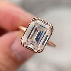 a close up of a person holding a ring with an emerald cut diamond in it