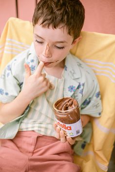 a young boy sitting on a bed eating chocolate and holding a peanut butter jar in his hand