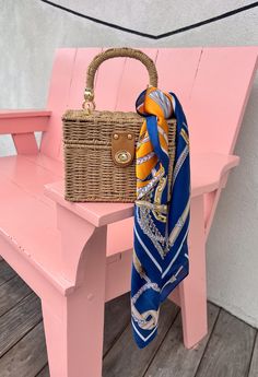 a purse sitting on top of a pink bench next to a wooden bench with a blue and yellow scarf hanging from it