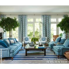 a living room with blue couches and chairs in front of two large windows that have potted plants on them