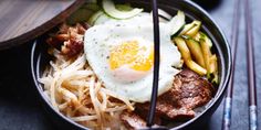 a bowl filled with meat, noodles and an egg on top of it next to chopsticks