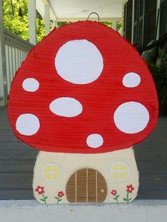 a red mushroom house with white polka dots on it's roof is sitting on the porch