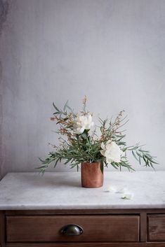 white flowers are in a copper vase on a marble table