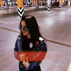 a young woman wearing sunglasses and holding a red object in front of an empty parking lot