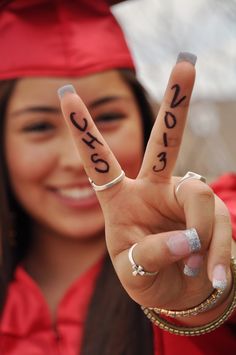 a woman in graduation cap and gown holding up two fingers with the word peace written on them