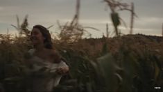 a woman is standing in the middle of a field with tall grass and looking up