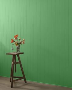 a wooden stool with flowers on it in front of a green wall and wood floor