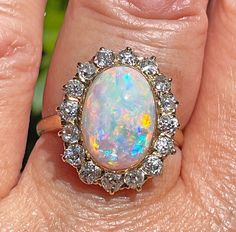 A magnificent turn-of-the-century late Victorian, early Edwardian Opal and Diamond Cluster 18k Gold ring, Circa 1900 This Crystal Australian opal displays electric play of color in a Oval shape. The confetti like pattern with all the colors of the rainbow: blue, yellow, sunset orange, turquoise, purple, green and red. The opal has a Gorgeous Array of All the Colors, depending on how the flashes of colors are viewed from different angles caused by the light that is infused into the stone.. No black dead spots or No gemological evidence of crazing is present! A delightful piece for an avid opal collector. The Center is Australian Crystal Opal is Simply Stunning, measuring approximately 14.40x10.21mm and 4.78ct ( estimated ), solid crystal, all natural with lots of fire and great brilliance. Yellow Sunset, Antique Jewelry Rings, Diamond Color Grade, Orange Turquoise, The Colors Of The Rainbow, Sunset Orange, Crystal Opal, Colors Of The Rainbow, 18k Gold Ring