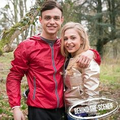 a man and woman standing next to each other in the woods with trees behind them