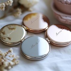 four personalized compact mirrors sitting on top of a white table with flowers in the background