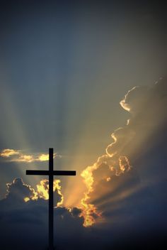 a cross with the sun shining behind it in front of some clouds and blue sky