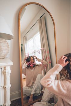 a woman sitting on the floor in front of a mirror holding her hair up to her head