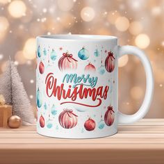 a white coffee mug with merry christmas ornaments on it next to a small wooden tree