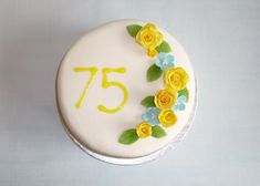 a white cake with yellow and blue flowers on it's side that says 75