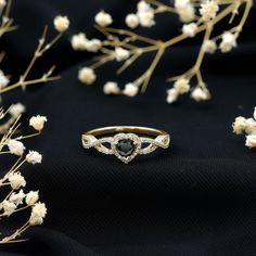 a black diamond ring sitting on top of a table next to white flowers and branches