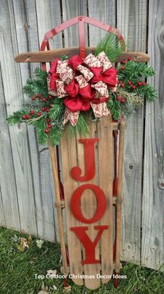 a wooden sled with the word joy in red and green decorations on it sitting next to a fence