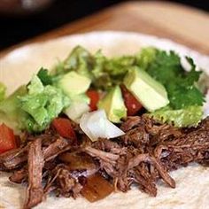 a tortilla with shredded meat, lettuce and tomatoes on it sitting on a cutting board