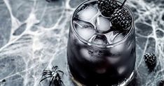 a glass filled with ice and blackberries on top of a marble table next to spider legs