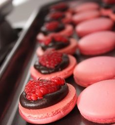 pink and black macaroons with raspberries on top are lined up in a row