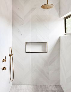 a white bathroom with herringbone tile and gold fixtures on the shower head, along with an open window