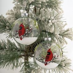 two christmas ornaments hanging from a tree with snow on it's branches and red cardinal sitting on the branch