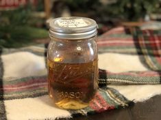 a mason jar filled with liquid sitting on top of a plaid table cloth next to a christmas tree