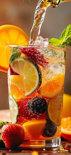 a glass filled with fruit and water being poured into it