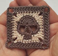 a hand holding a small crocheted square in the shape of a skull on it