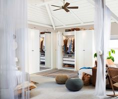 a bedroom with white walls and ceiling fan, bed, chair and closet doors open