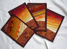 four quilted coasters are arranged on a white tablecloth with orange, yellow and red colors