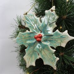 a ceramic christmas ornament hanging from a tree branch with red berries on it