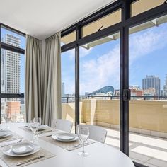 the dining table is set with white plates and silverware in front of large windows