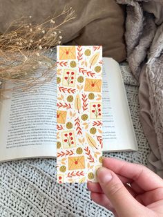 a person is holding an open book in front of a blanket with flowers and leaves on it