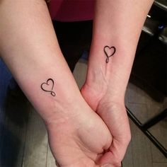 two people holding hands with small tattoos on their wrist and one has a heart in the middle