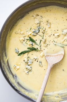 a wooden spoon in a pot filled with cheese and herbs