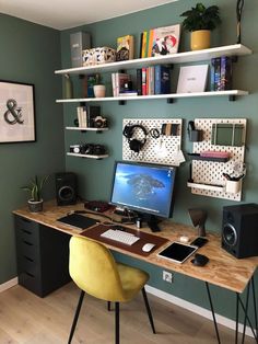 a desk with a computer, speakers and bookshelves on it in front of a green wall