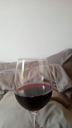 a glass of red wine sitting on top of a bed next to a person's hand