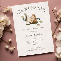 an open book on top of a table next to some white flowers and greenery