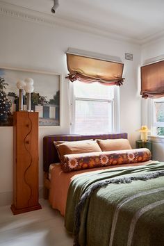 a bed sitting under a window next to a wooden dresser in a room with white walls