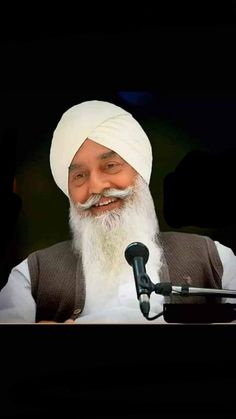 an old man with a long white beard wearing a turban and speaking into a microphone