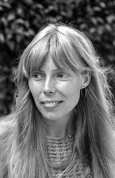 a black and white photo of a woman with long blonde hair wearing a sweater in front of some bushes