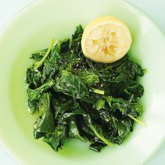 a green plate topped with spinach and a slice of lemon wedged into it