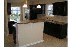 an empty kitchen with black cabinets and marble counter tops, along with two pendant lights hanging from the ceiling