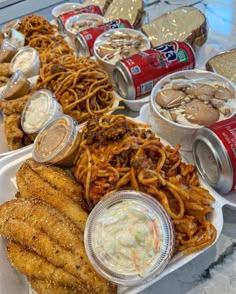 an assortment of food items on a table with cans of beer and other foods in the background