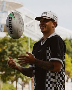 a man in checkered shirt tossing a white and black rugby ball on his hand