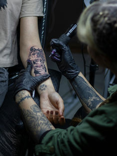 two people with tattoos on their arms are getting ink done by one person who is holding the other's hand