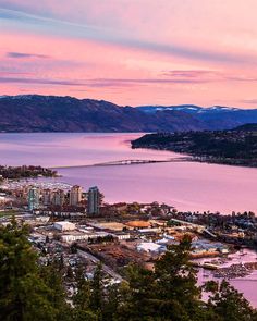 an aerial view of a city and the ocean at sunset with mountains in the background