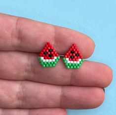 a pair of small red, green and white watermelon studs on a person's hand