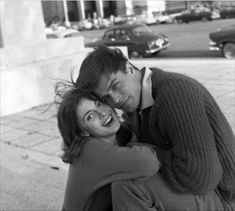 black and white photograph of two people hugging each other on the sidewalk in front of a building